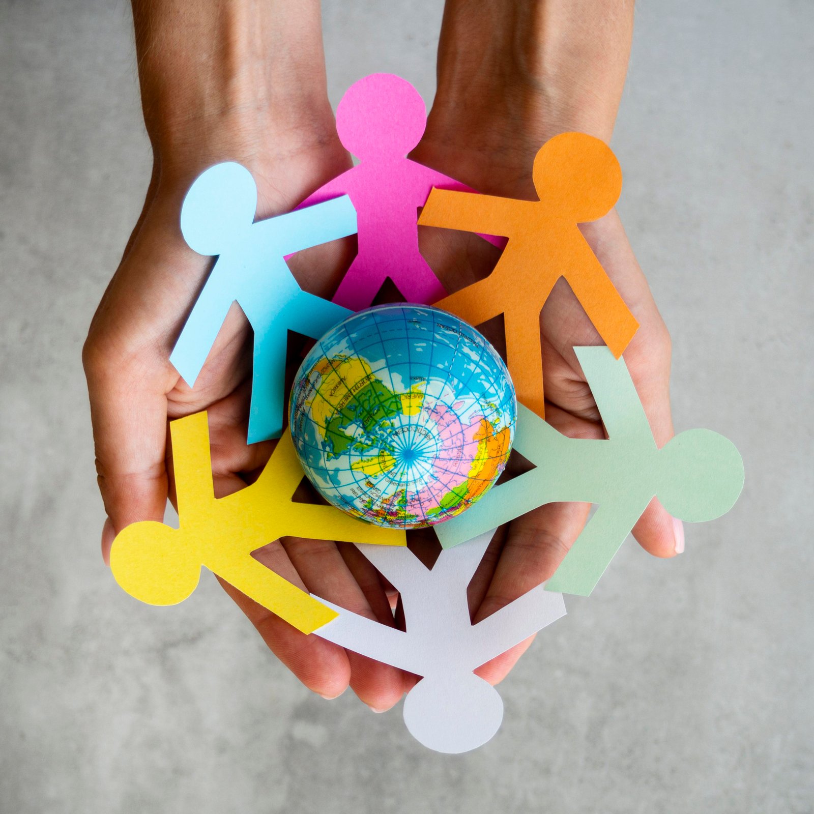 Figuras de papel de colores tomadas de la mano alrededor de un globo terráqueo, símbolo de alianzas globales